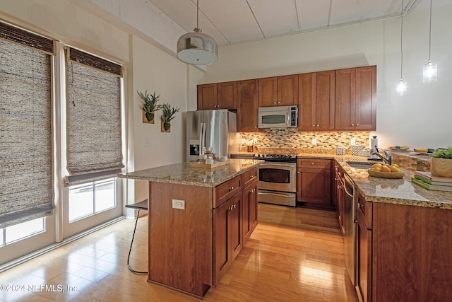 kitchen with pendant lighting, sink, decorative backsplash, light stone countertops, and stainless steel appliances