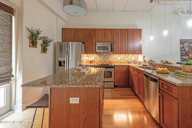 kitchen with pendant lighting, sink, stone countertops, a kitchen bar, and stainless steel appliances