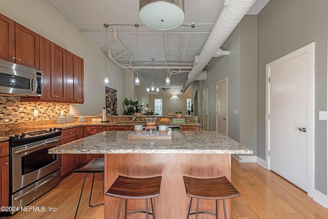 kitchen with light stone countertops, stainless steel appliances, tasteful backsplash, light hardwood / wood-style floors, and a breakfast bar