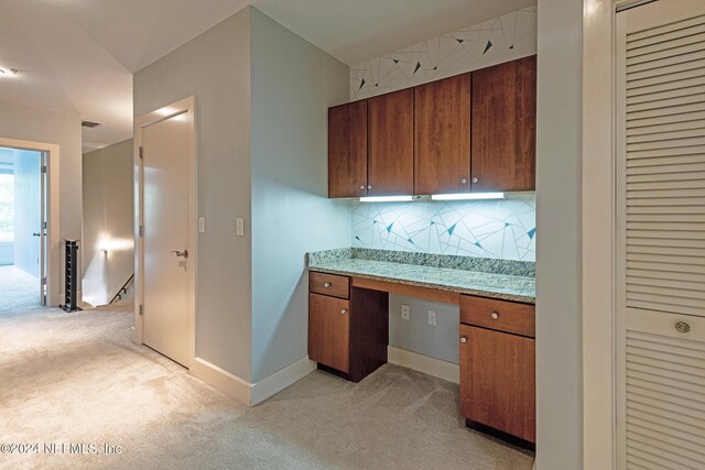 kitchen with built in desk, tasteful backsplash, light stone counters, and light colored carpet