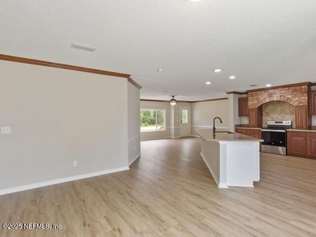 kitchen with stainless steel range with electric stovetop, a center island with sink, sink, light hardwood / wood-style flooring, and ornamental molding