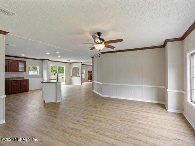 unfurnished living room with ceiling fan, ornamental molding, a textured ceiling, and light hardwood / wood-style flooring