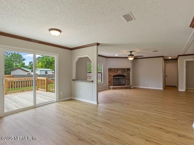 unfurnished living room featuring ornamental molding, a textured ceiling, ceiling fan, light hardwood / wood-style flooring, and a stone fireplace