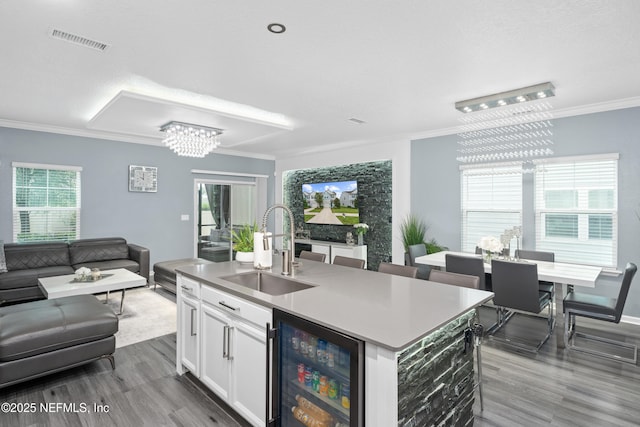 kitchen with wine cooler, a kitchen island with sink, sink, a notable chandelier, and white cabinetry