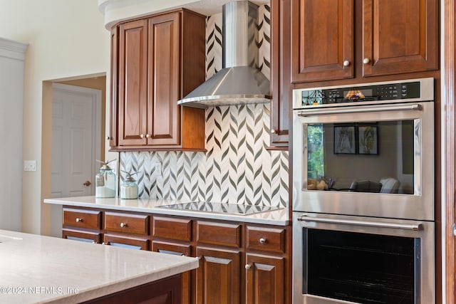 kitchen with decorative backsplash, black electric stovetop, wall chimney exhaust hood, and stainless steel double oven