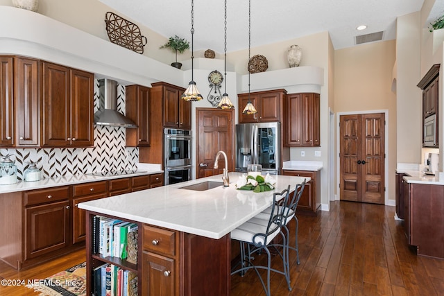 kitchen with wall chimney exhaust hood, stainless steel appliances, an island with sink, pendant lighting, and decorative backsplash