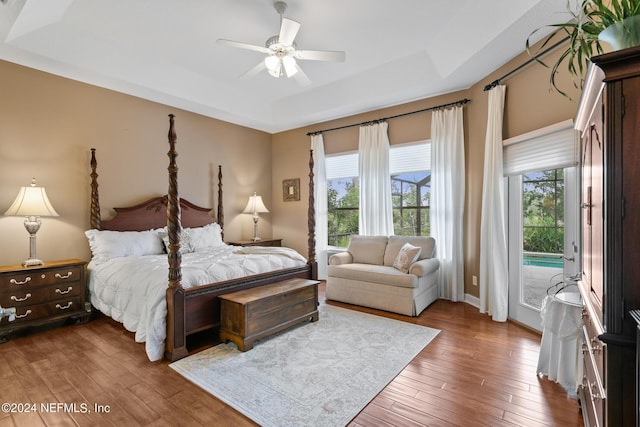 bedroom featuring access to outside, ceiling fan, a tray ceiling, and dark hardwood / wood-style floors