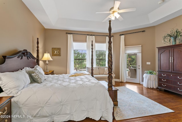 bedroom with a tray ceiling, access to exterior, ceiling fan, and dark hardwood / wood-style floors