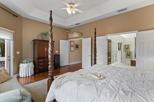 bedroom featuring ceiling fan, a raised ceiling, wood-type flooring, and ensuite bath