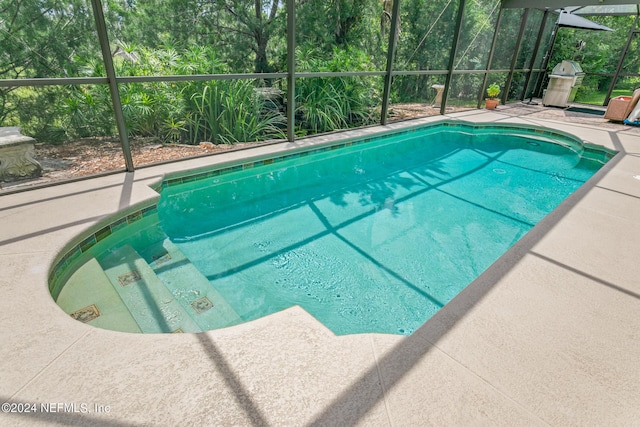 view of swimming pool featuring area for grilling, a patio, and glass enclosure