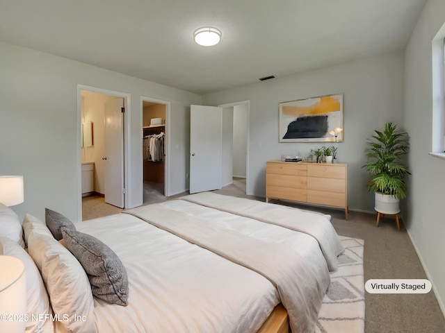 bedroom featuring connected bathroom, a spacious closet, a closet, and light carpet