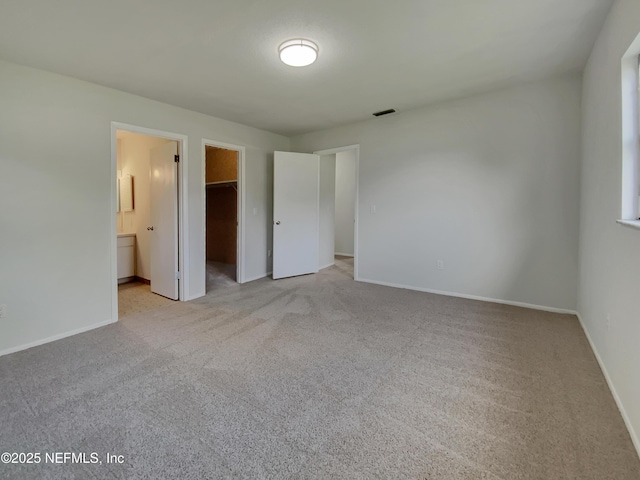 unfurnished bedroom featuring connected bathroom, a spacious closet, a closet, and light carpet