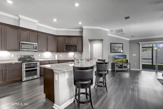 kitchen with appliances with stainless steel finishes, a kitchen breakfast bar, a textured ceiling, sink, and a center island with sink