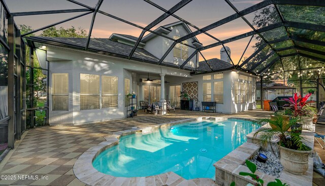 pool at dusk featuring a lanai, a patio area, and ceiling fan