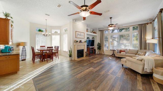 tiled living room featuring a textured ceiling, ceiling fan with notable chandelier, and a healthy amount of sunlight