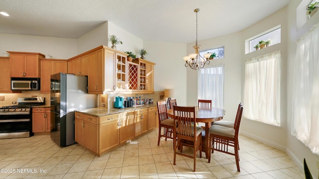 kitchen featuring light stone countertops, decorative backsplash, stainless steel appliances, a notable chandelier, and light tile patterned flooring