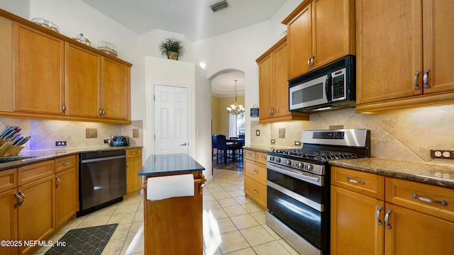 kitchen with dishwasher, stainless steel gas range oven, backsplash, dark stone counters, and light tile patterned floors