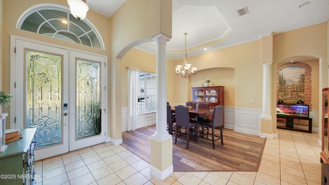 entryway with french doors, a raised ceiling, a chandelier, light tile patterned floors, and ornamental molding