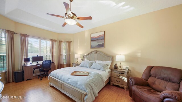 bedroom featuring ceiling fan, a raised ceiling, and light wood-type flooring