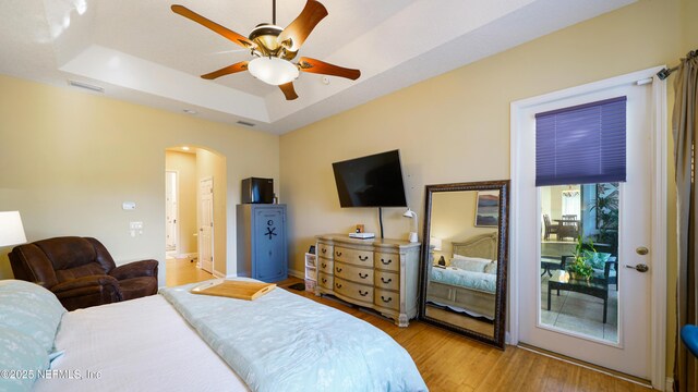 bedroom featuring access to exterior, light hardwood / wood-style flooring, a raised ceiling, and ceiling fan