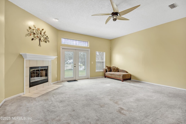 unfurnished room featuring light carpet, french doors, a textured ceiling, ceiling fan, and a fireplace