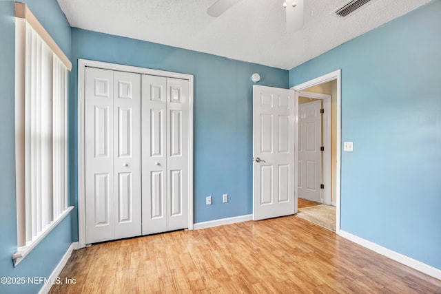 unfurnished bedroom featuring a textured ceiling, a closet, light hardwood / wood-style flooring, and ceiling fan