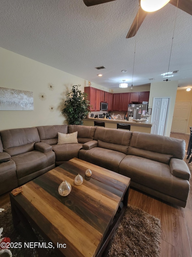 living room featuring ceiling fan, hardwood / wood-style floors, and a textured ceiling