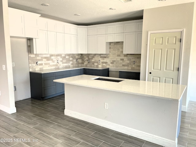 kitchen featuring tasteful backsplash, a kitchen island, baseboards, wood tiled floor, and white cabinetry