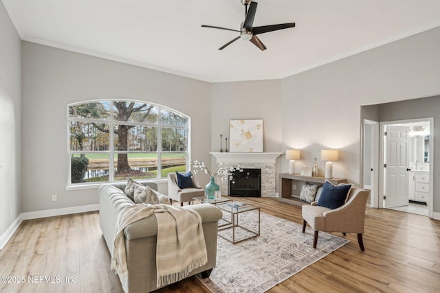 living room featuring ceiling fan, wood-type flooring, crown molding, and a stone fireplace