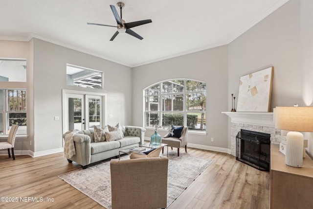 living room featuring french doors, a fireplace, ceiling fan, light hardwood / wood-style flooring, and crown molding