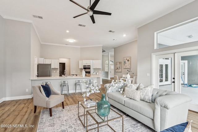 living room featuring ceiling fan, light wood-type flooring, french doors, crown molding, and sink