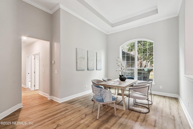 dining room featuring a raised ceiling, light wood-type flooring, and ornamental molding