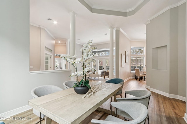 dining room with hardwood / wood-style floors, ornate columns, french doors, a raised ceiling, and ornamental molding