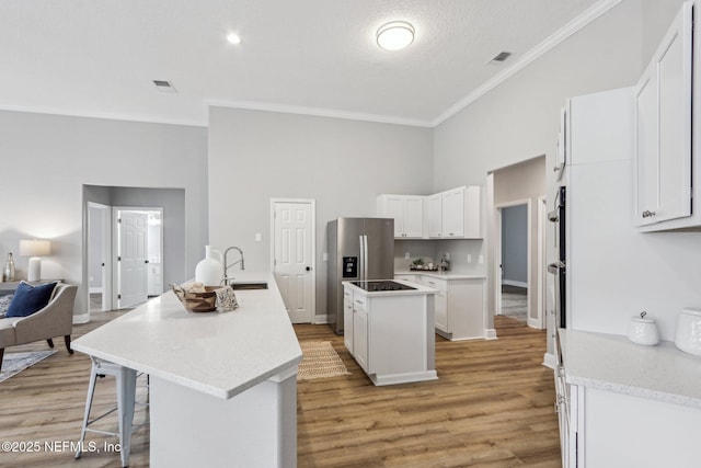 kitchen featuring stainless steel fridge, a center island with sink, a textured ceiling, white cabinets, and sink