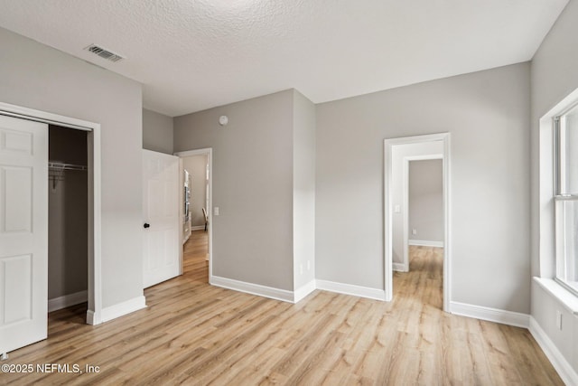 unfurnished bedroom featuring a textured ceiling, a closet, and light hardwood / wood-style flooring