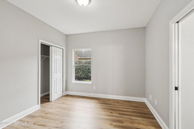 unfurnished bedroom with light hardwood / wood-style floors, a textured ceiling, and a closet