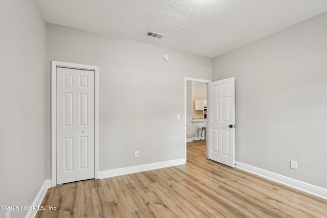 unfurnished bedroom with a textured ceiling, a closet, and light wood-type flooring