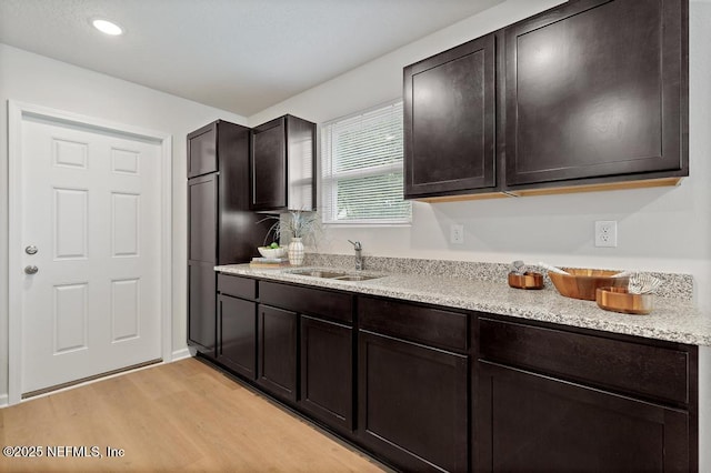 kitchen featuring light wood-type flooring, dark brown cabinetry, light stone counters, and sink