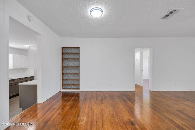 unfurnished living room with built in features, dark wood-type flooring, and a textured ceiling