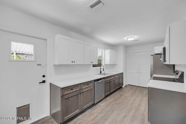 kitchen featuring dishwasher, stove, white cabinets, sink, and light wood-type flooring