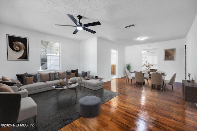 living room featuring a textured ceiling, ceiling fan, and dark wood-type flooring