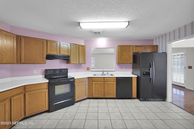 kitchen with sink, light tile patterned floors, black appliances, and a textured ceiling