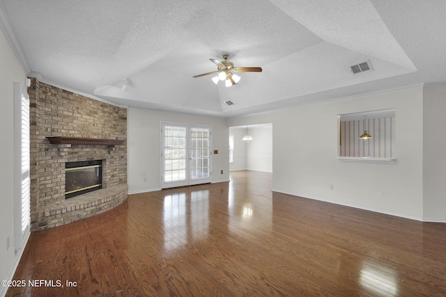 unfurnished living room with a tray ceiling, ceiling fan, dark hardwood / wood-style flooring, and a brick fireplace