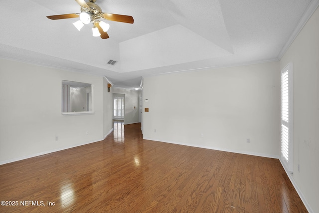 empty room featuring a tray ceiling, a wealth of natural light, ceiling fan, and wood-type flooring