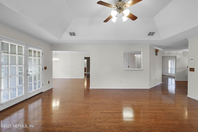 empty room featuring french doors, dark wood-type flooring, a raised ceiling, crown molding, and ceiling fan with notable chandelier