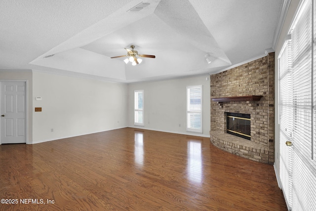 unfurnished living room featuring a tray ceiling, dark hardwood / wood-style floors, a textured ceiling, and a brick fireplace