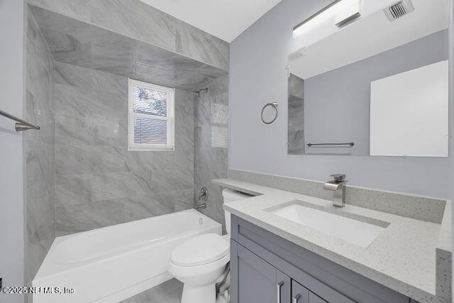 full bathroom with vanity, tiled shower / bath combo, and toilet