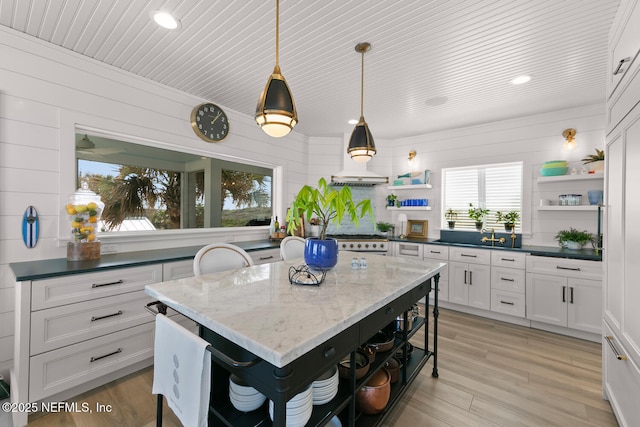 kitchen featuring white cabinets, hanging light fixtures, light hardwood / wood-style floors, and wooden walls