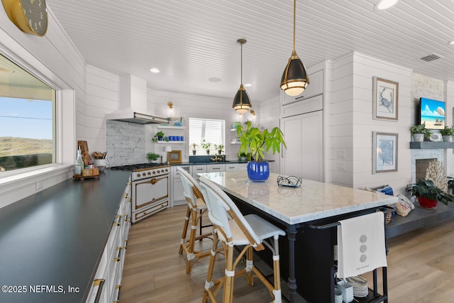 kitchen with white cabinets, a kitchen bar, white range with gas stovetop, wall chimney range hood, and pendant lighting