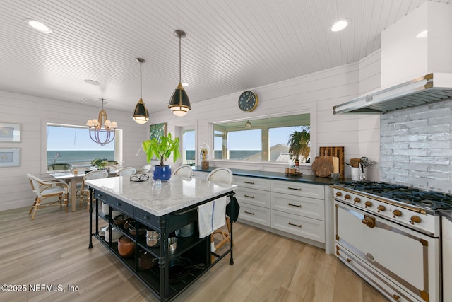 kitchen featuring pendant lighting, wall chimney range hood, white range, white cabinetry, and dark stone countertops